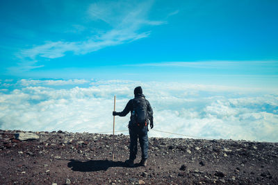 Rear view of hiker standing on mountain against cloudscape