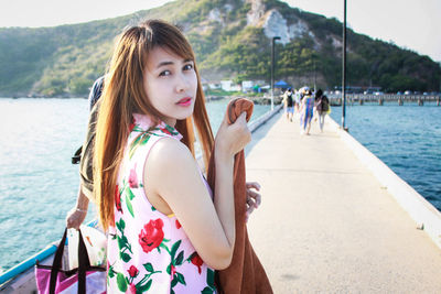 Portrait of beautiful woman standing on walkway amidst sea