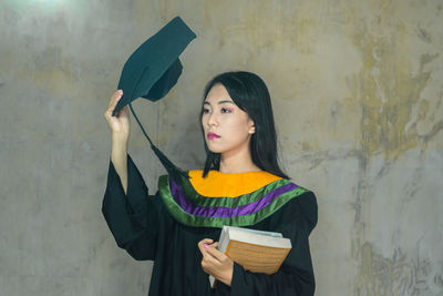 Young woman holding umbrella standing against wall