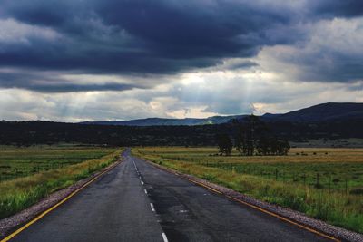 Empty road amidst field against sky