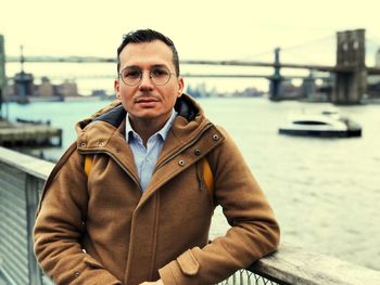 Portrait of mid adult man wearing warm clothing while standing by river in city