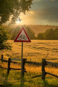 Road sign by trees on field against sky