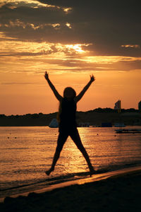 Black silhouette of a female kid jumping in the air in the shape of an x with shiny evening sky