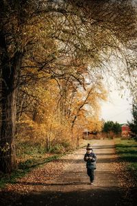 Rear view of man cycling on road amidst trees during autumn