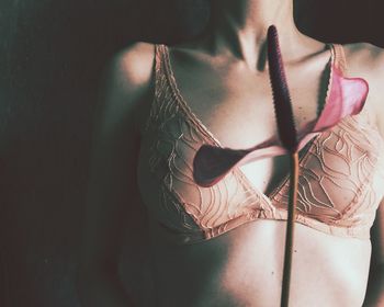 Midsection of sensuous woman with pink flower in darkroom