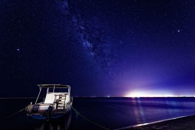 Boat moored at scenic illuminated sea against sky during night