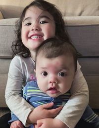 Portrait of cute smiling sisters sitting on sofa at home