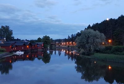 Scenic view of lake by illuminated buildings against sky