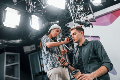 Young man is preparing for tv online broadcast. woman helps with make up.