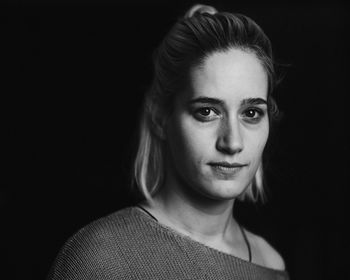 Close-up portrait of smiling young woman against black background