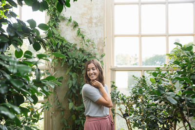 Portrait of smiling young woman standing against window