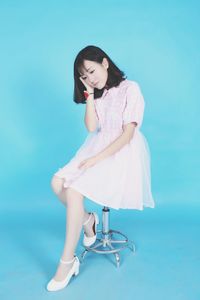 Young beautiful woman sitting on chair against blue background