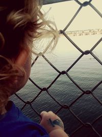 Portrait of woman by sea seen through fence