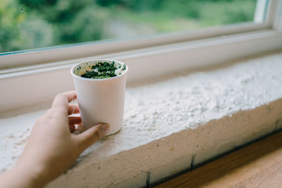 Midsection of person holding ice cream on window sill