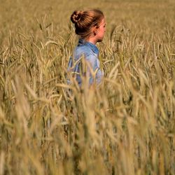 Side view of teenage girl standing amidst plants in farm