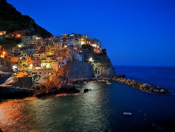 Illuminated buildings by sea against clear blue sky