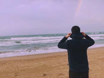 Rear view of man looking at sea against sky during sunset