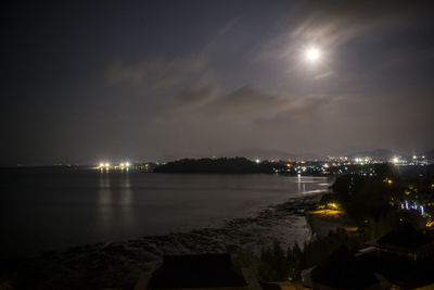 Illuminated city by sea against sky at night