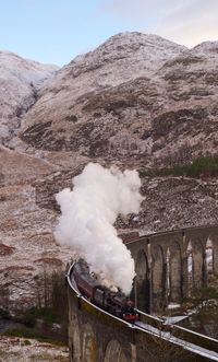 Smoke emitting from bridge over mountain against sky