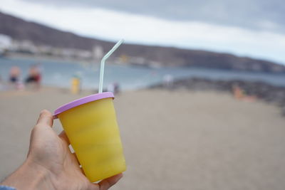 Midsection of person holding yellow umbrella on beach