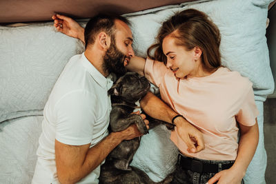 Happy couple man and woman laying on the bed with their dog, french bulldog sleeping with humans