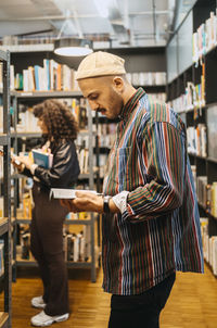 Side view of man reading book by woman in library at community college