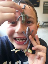 Close-up portrait of smiling boy holding toy lizards at home