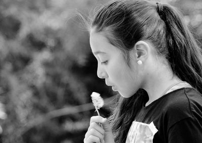 Close-up of girl blowing dandelion while standing outdoors