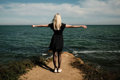 Blonde girl from the back in a black dress on a cliff over the sea. high quality photo