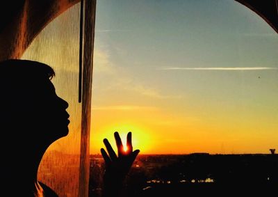 Low angle view of human hand against sky at sunset