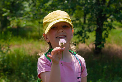 Positive emotional child smiles looks on pink flower in hand. cheerful pretty girl in yellow cap.