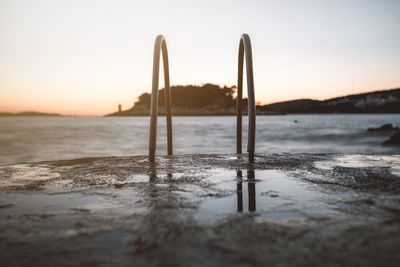 Wooden posts on beach against sky during sunset