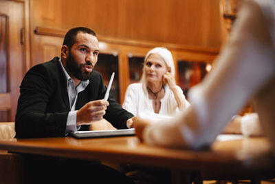 Confident male financial advisor discussing over contract document with female colleagues in board room