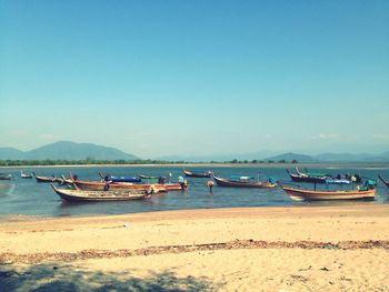 Boats moored in sea at beach against clear sky