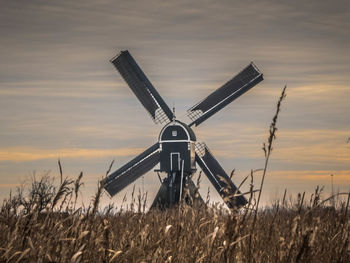 Traditional windmill on field against sky during sunset