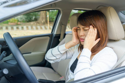 Young woman suffering from headache sitting in car