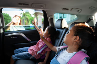 Mother waving hand to kids sitting in car