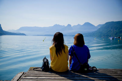 Rear view of women sitting on jetty against sky