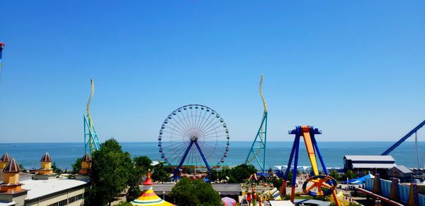 Ferris wheel by sea against clear blue sky