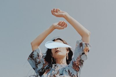 Low angle portrait of woman with arms raised against sky