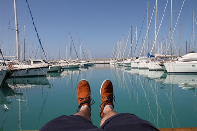 Low section of man against moored boats on sea