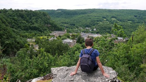 Rear view of boy with backpack sitting on cliff against landscape