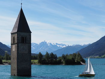 Tower of church and boat on lago di resia - italy scenic view of church by mountains against sky