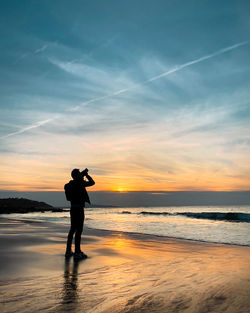 Silhouette woman standing at beach against sky during sunset