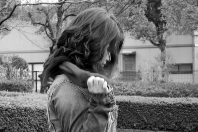 Side view of woman holding scarf while standing by hedge