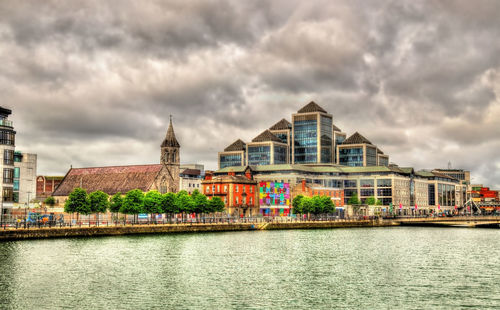 View of buildings by river against cloudy sky
