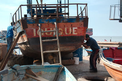 Man working on fishing boat against sky