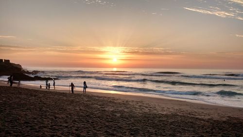 Silhouette people at beach against sky during sunset