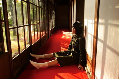 Side view of woman sitting on floor by window