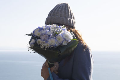 Portrait of woman with pink flower against sky